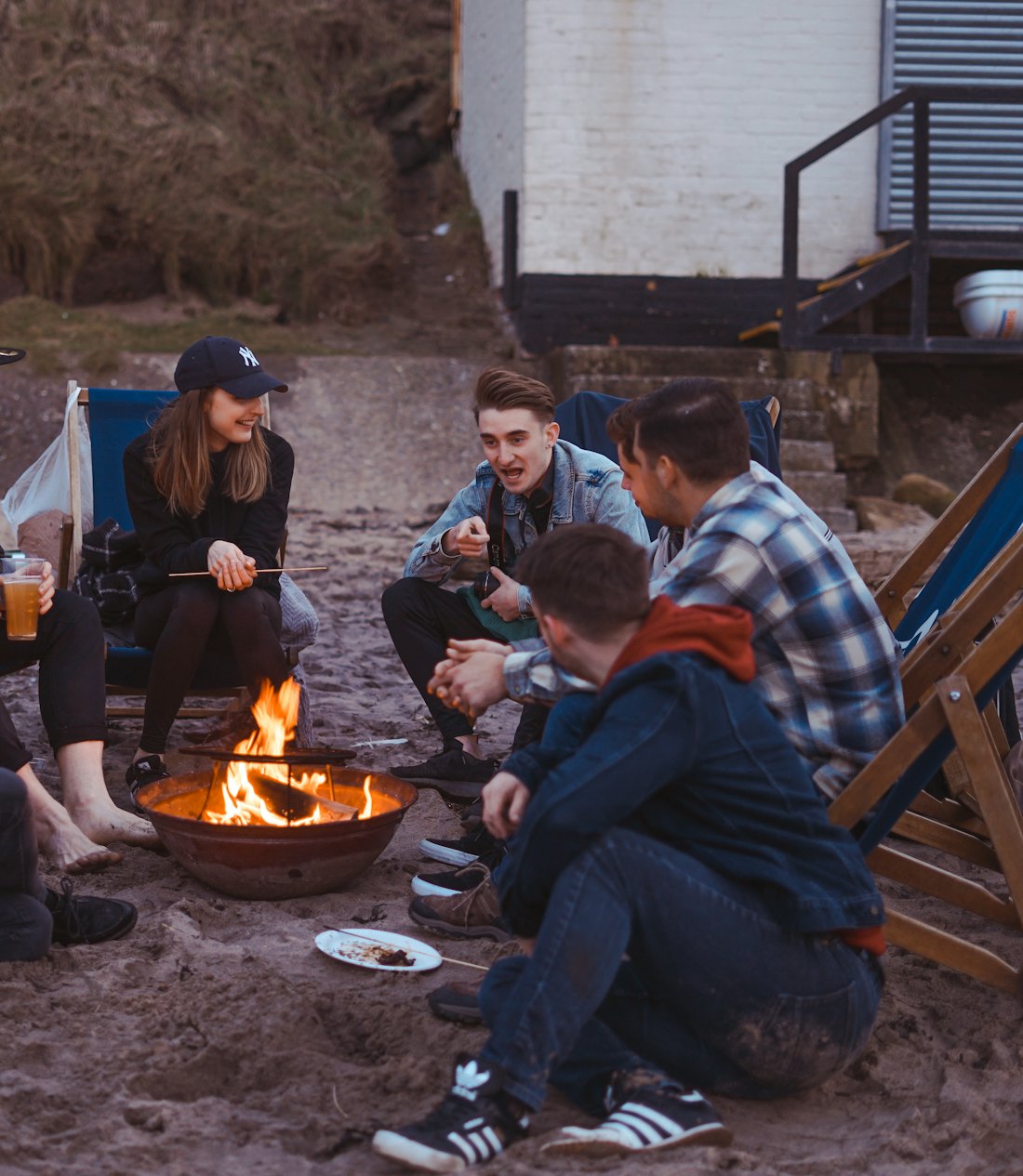 A group of friends laughing around a fire pit at dusk